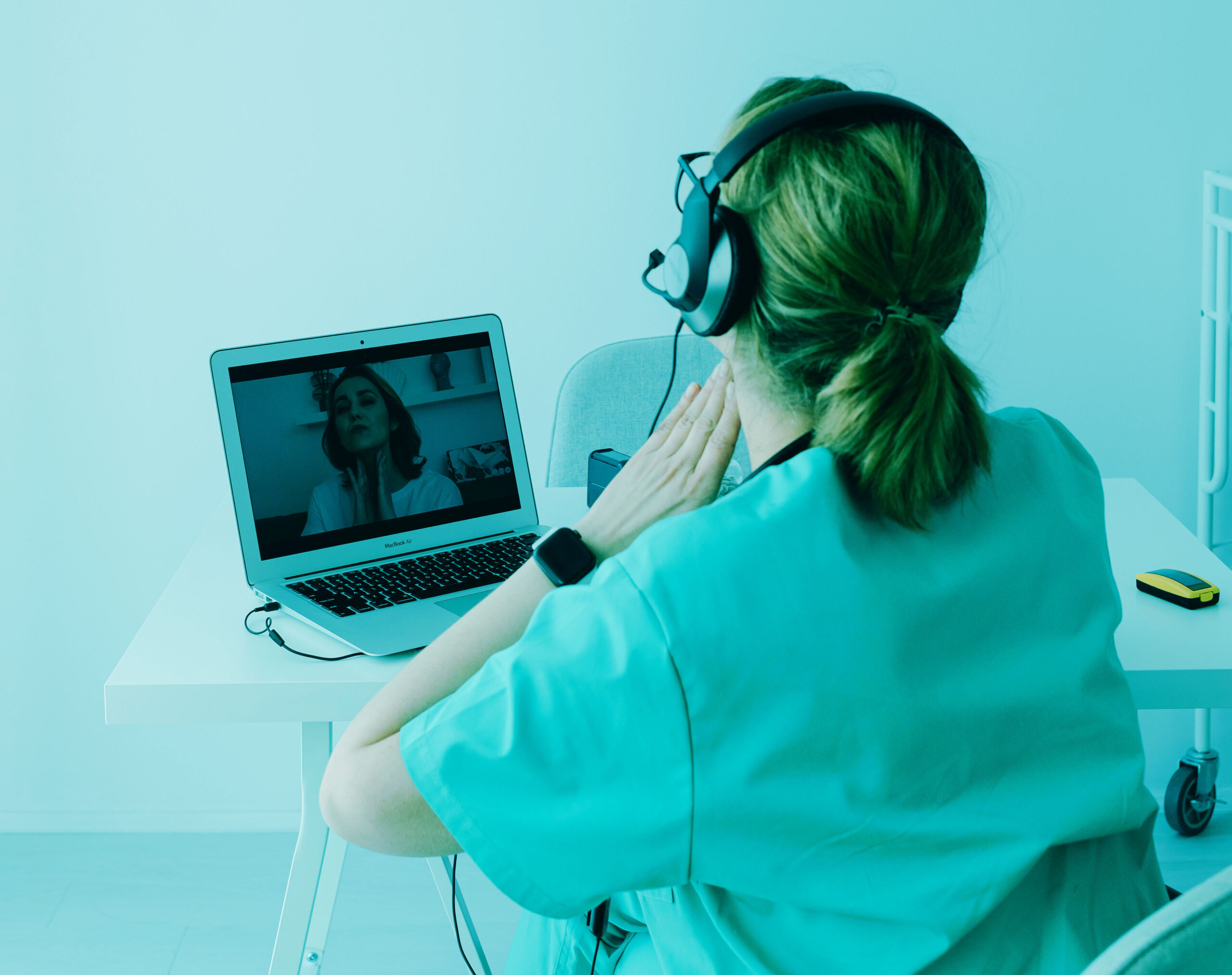 A medical professional wearing earphones consults with a patient via her laptop.