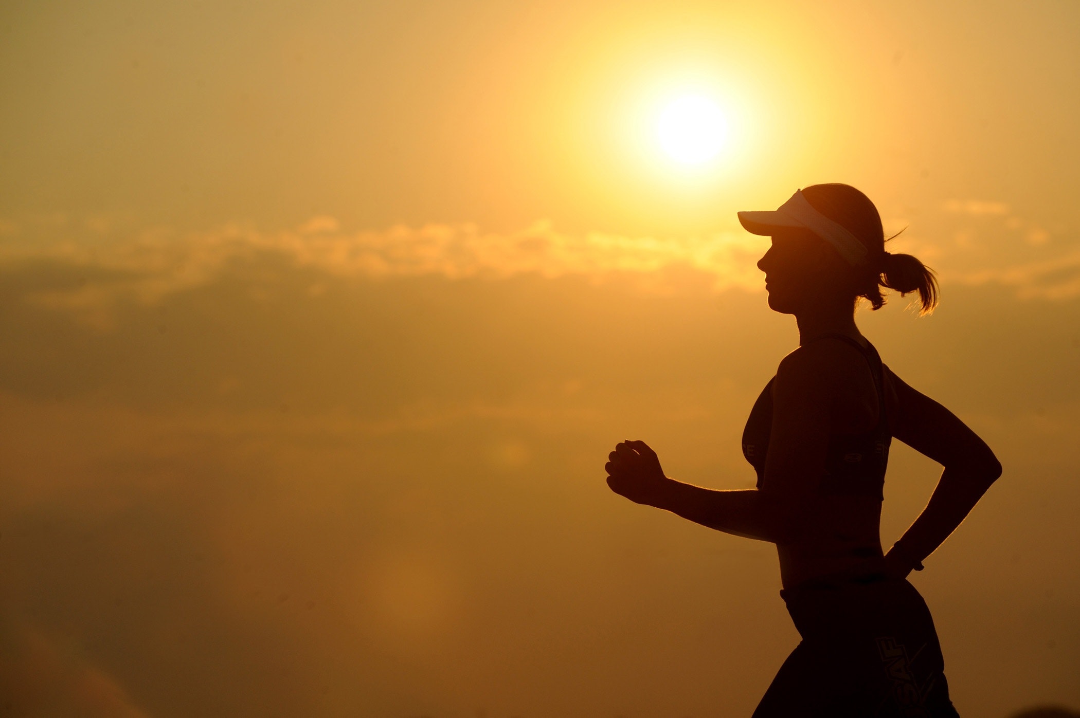 Silhouette of a woman running against an orange sunset